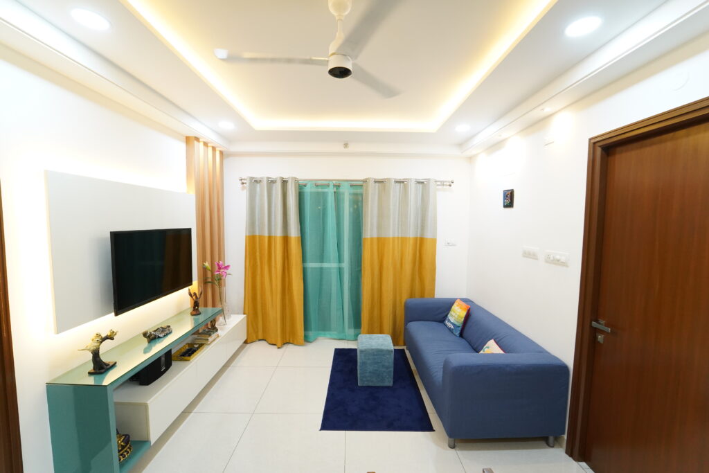 A living room with a blue couch and yellow curtains, expertly designed by interior designers -Dream Modular